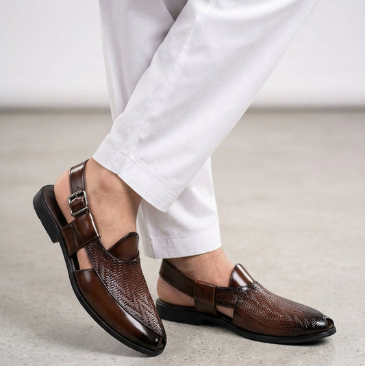 Brown dress shoes with patterned design held by a hand on a light gray background