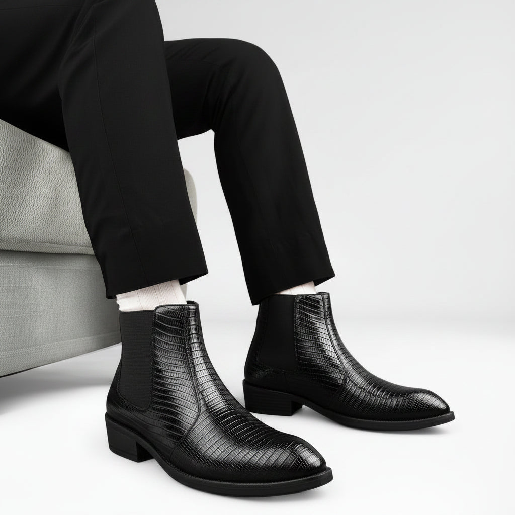 Black leather boots with a textured pattern worn by a person sitting on a couch.