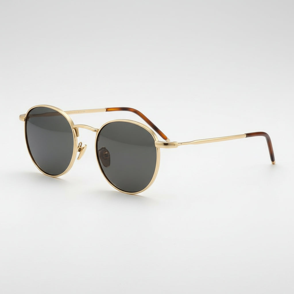 Oval sunglasses with gold metal frames, dark gray lenses, and tortoiseshell temple arms, shown on a clean light gray background.