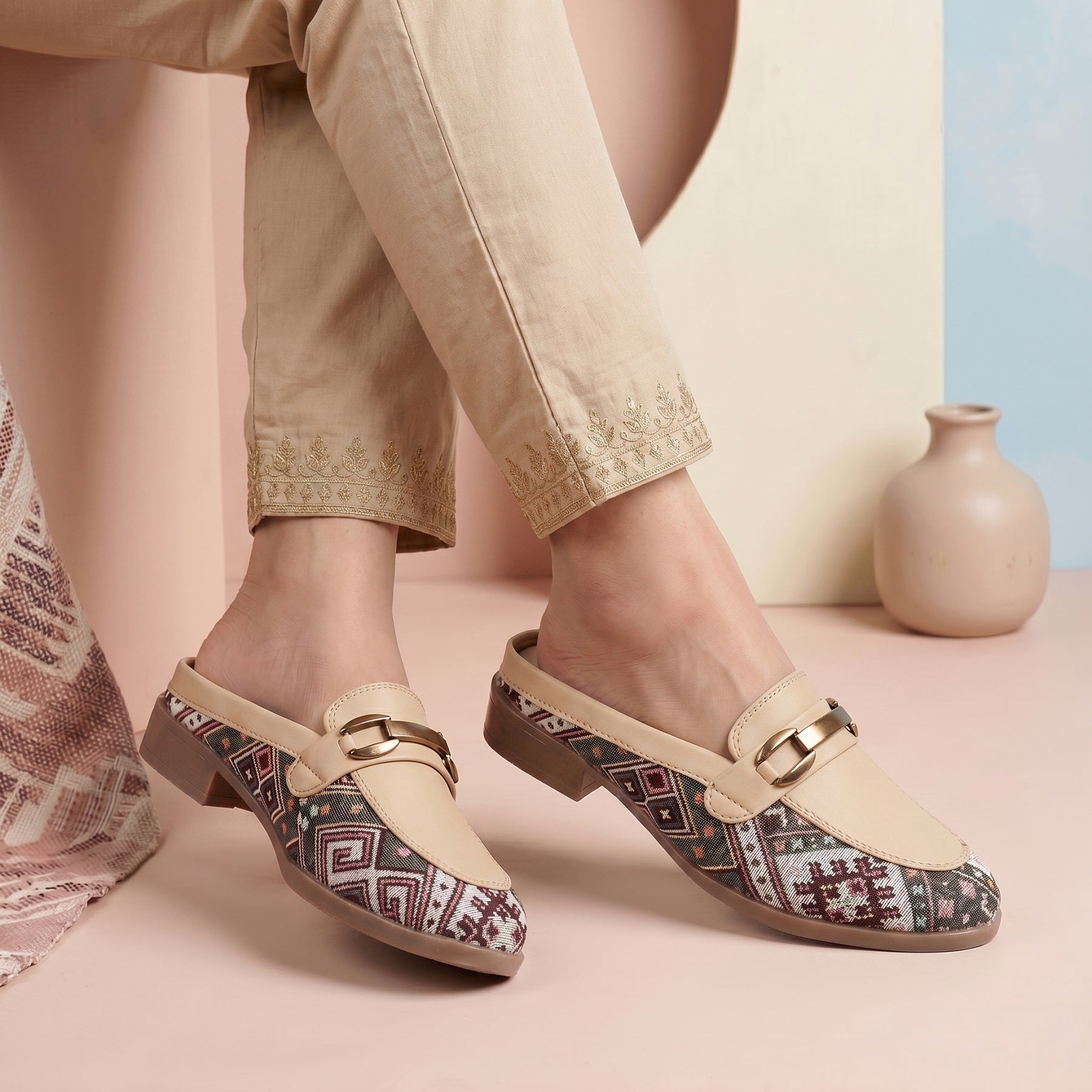 Person wearing patterned clogs with beige pants on a pastel background