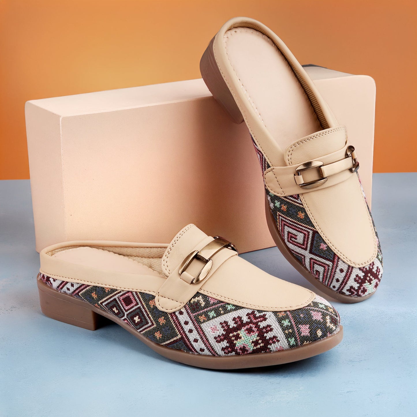 Pair of loafers with patterned toe and beige body on a blue and orange gradient background