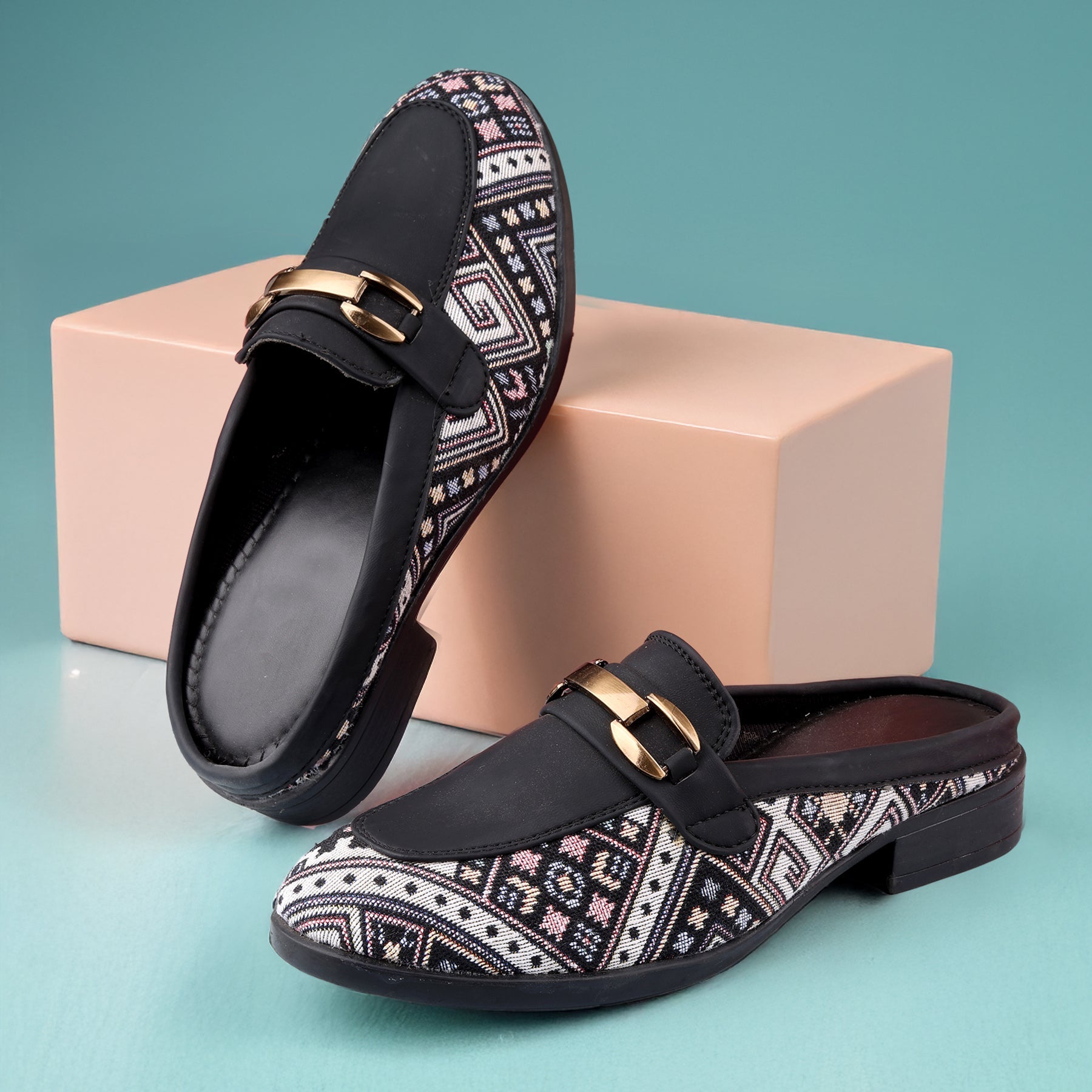Pair of black loafers with patterned straps and gold buckles on a teal background