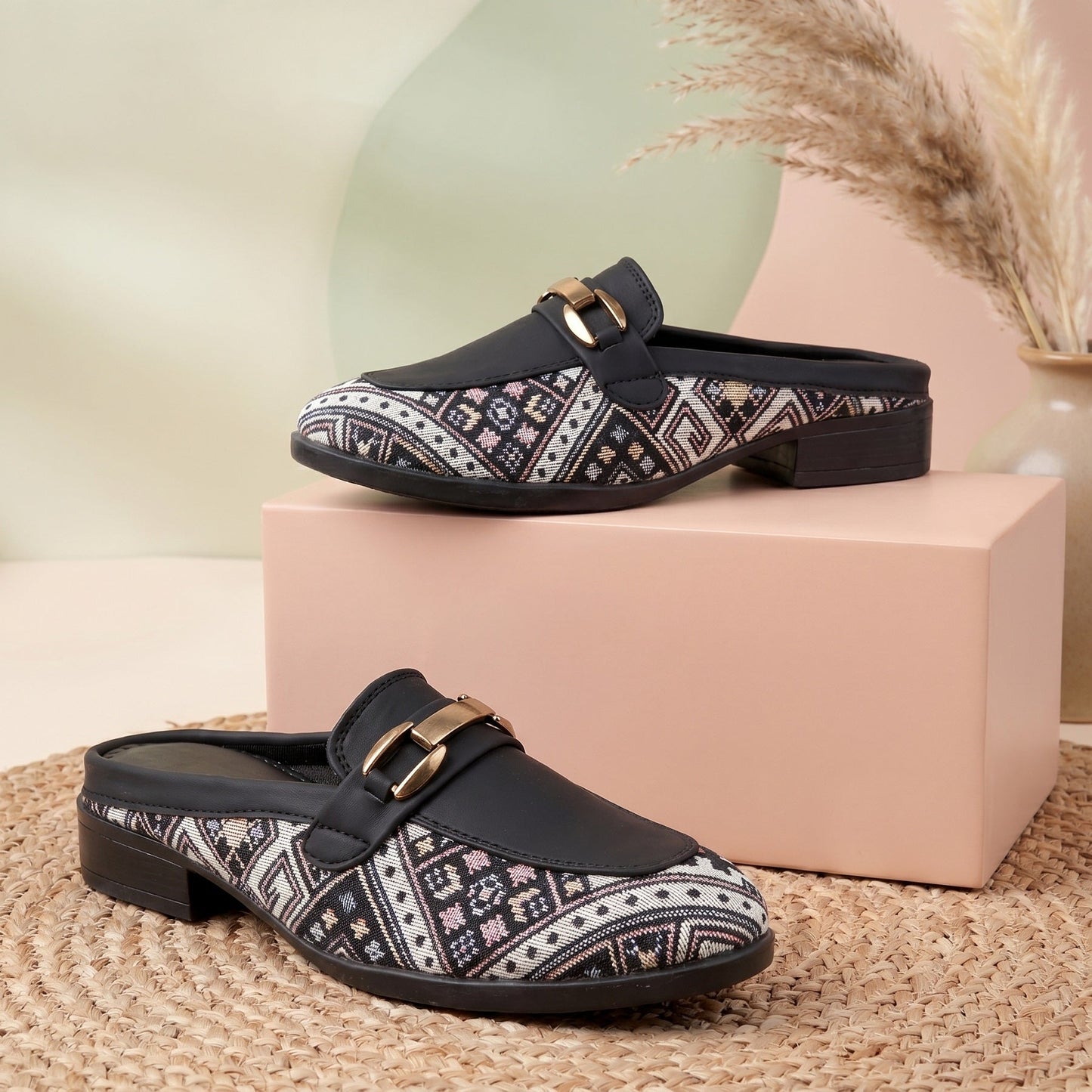 Pair of black patterned clogs on a pink box with a neutral background