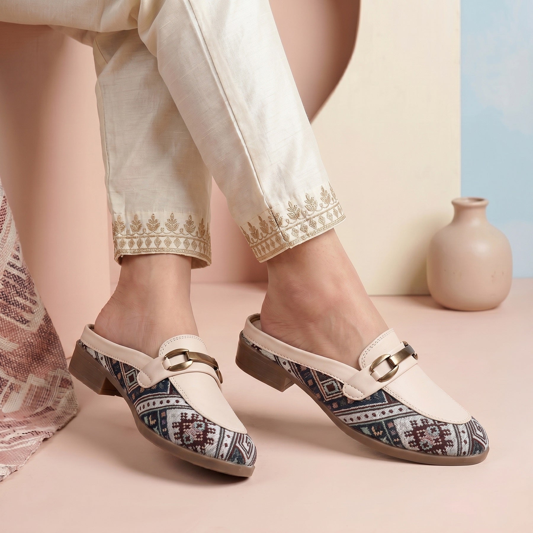 Pair of patterned shoes worn with white pants on a pastel background