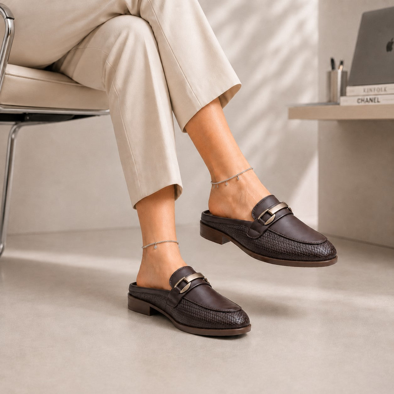 Person wearing dark brown loafers with metallic accents, sitting on a chair.