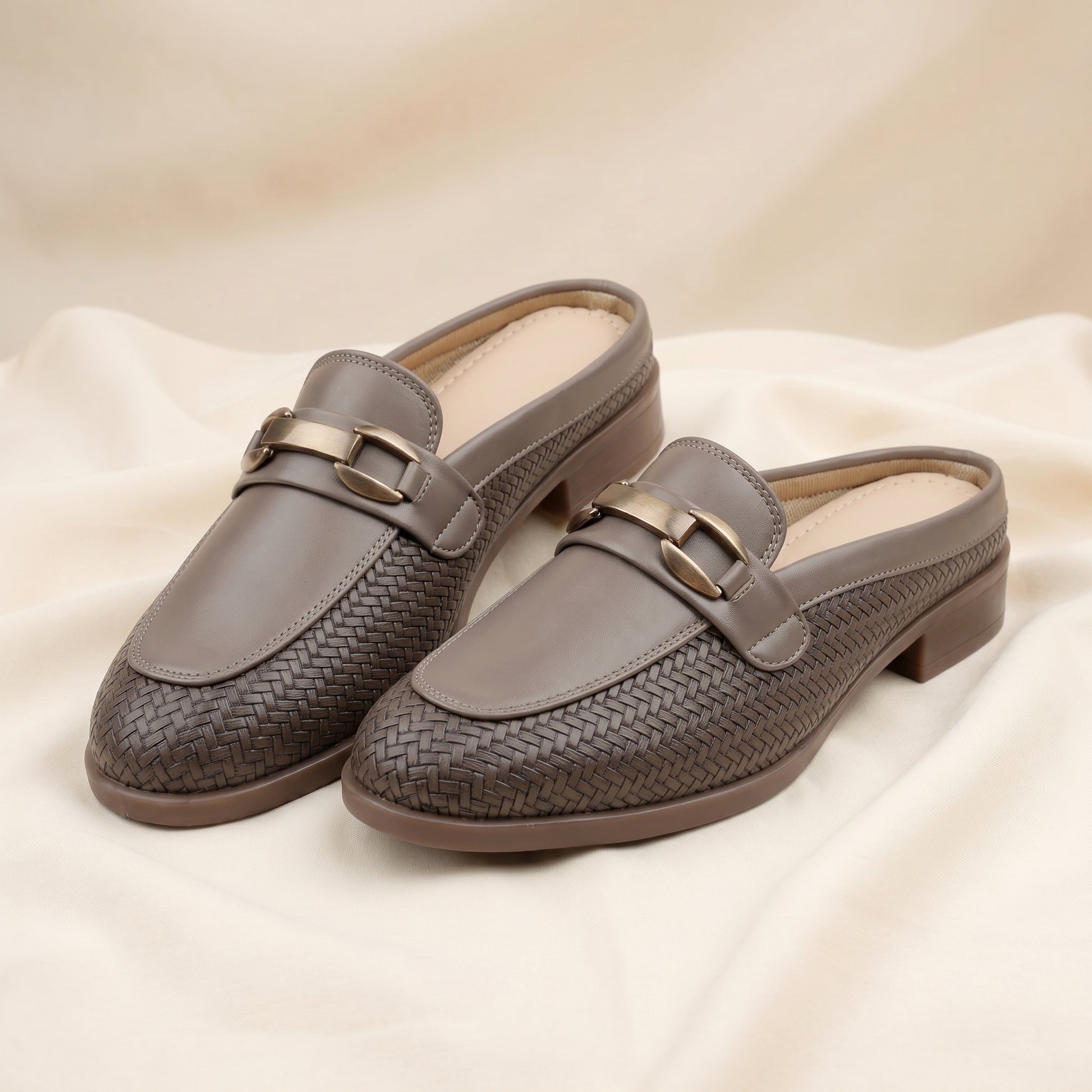 Pair of gray loafers with woven pattern on a beige fabric background