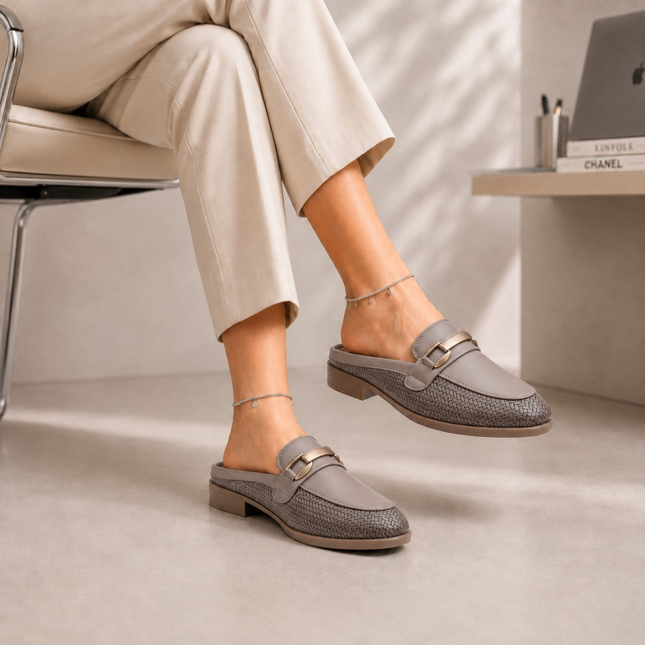 Person wearing gray loafers sitting on a chair with a neutral background