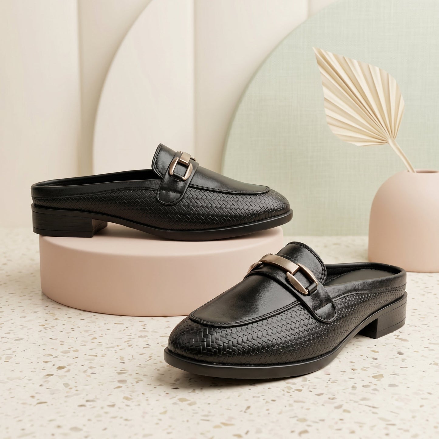 Black woven loafers on a textured surface with a neutral background