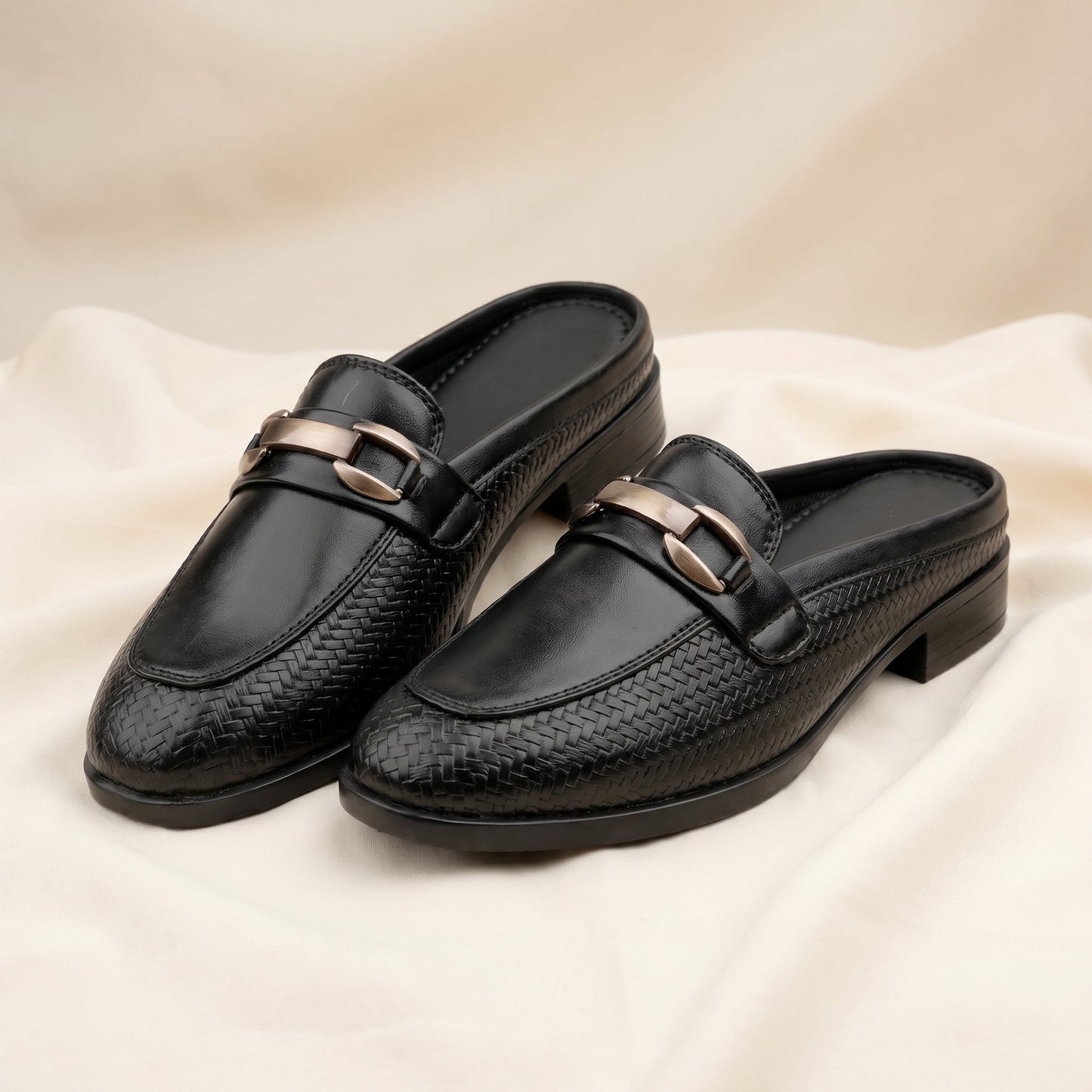 Pair of black loafers with gold buckles on a beige fabric background