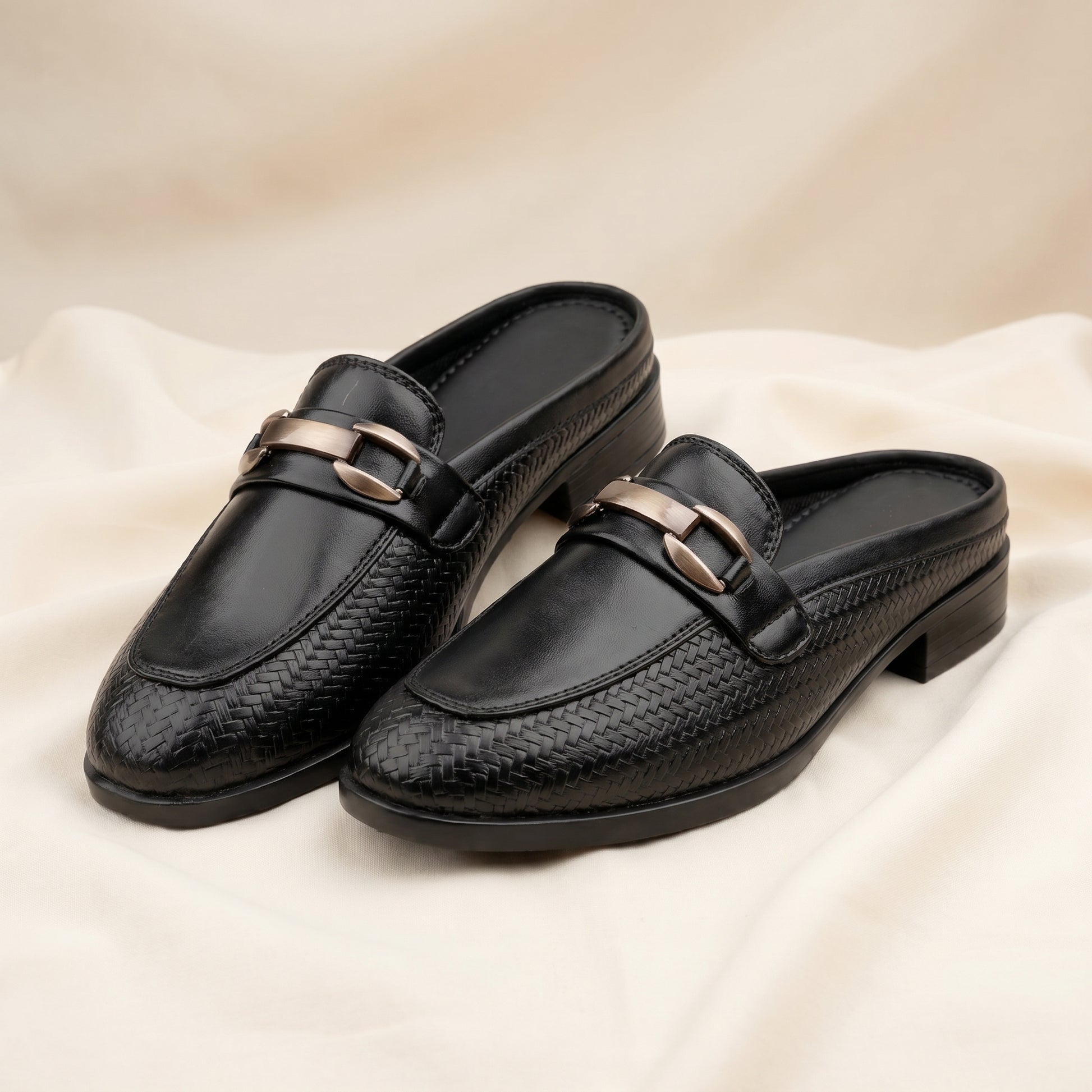 Pair of black loafers with gold buckles on a beige fabric background
