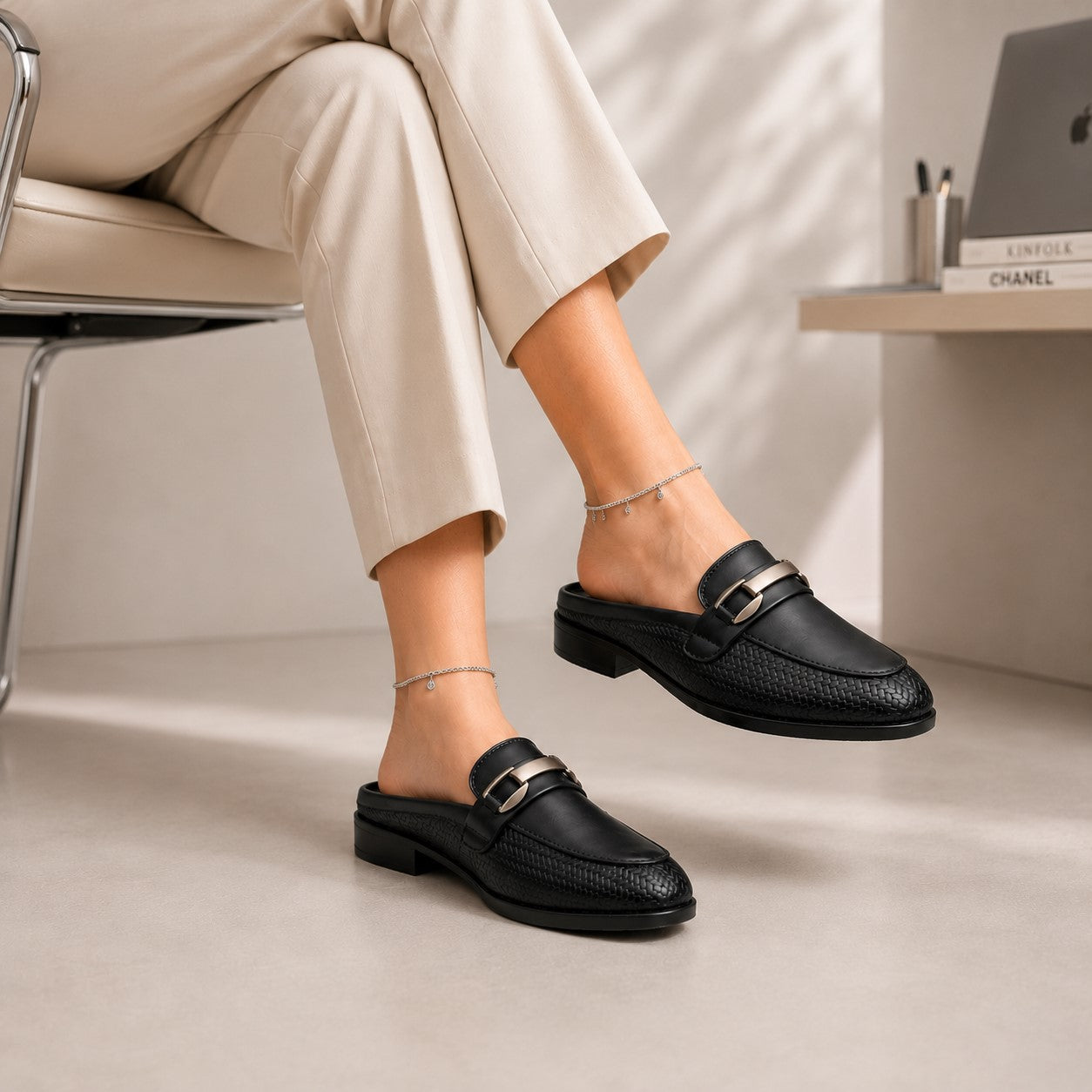 Person wearing black loafers with gold accents, sitting on a chair in a minimalistic setting.