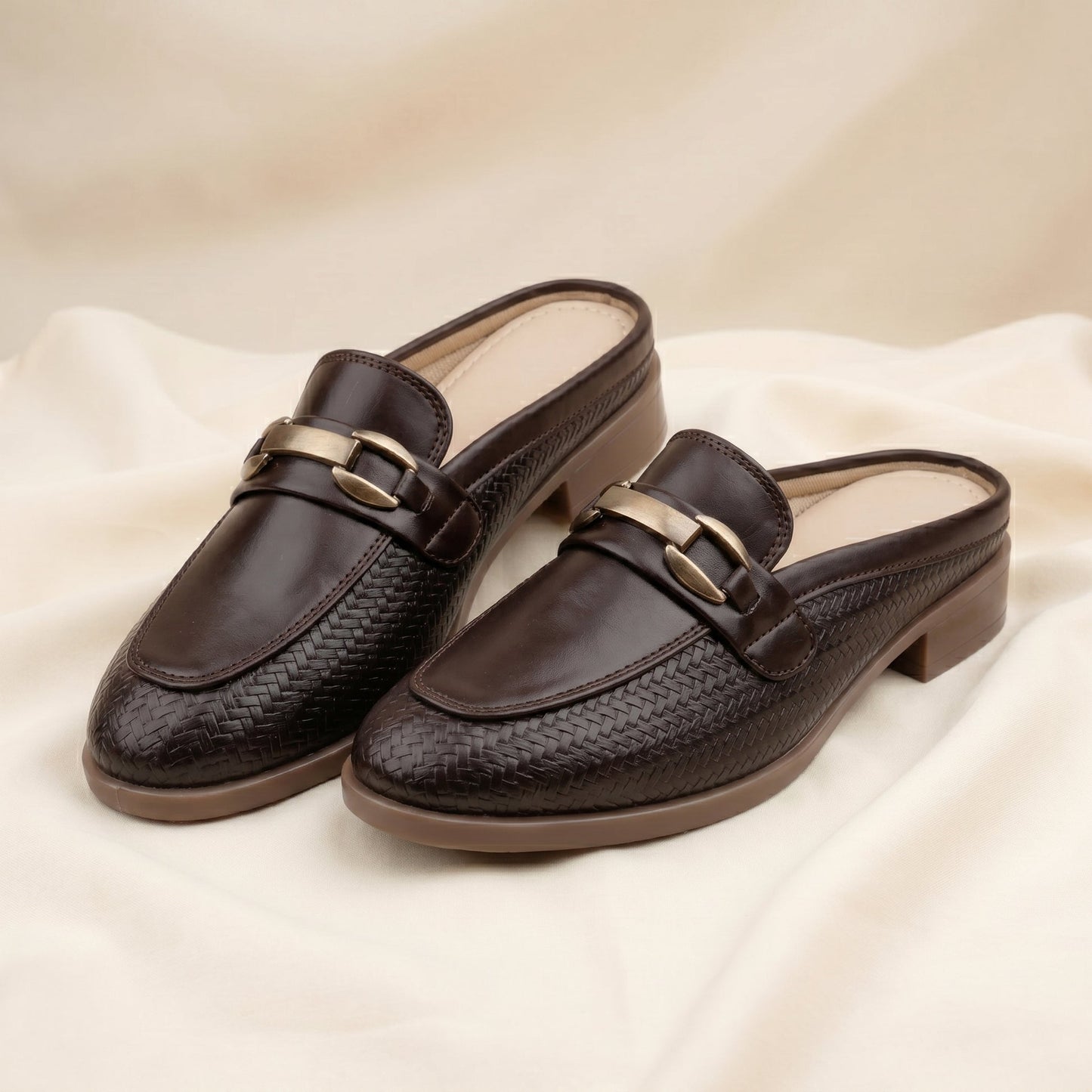Pair of brown loafers with gold buckles on a beige fabric background