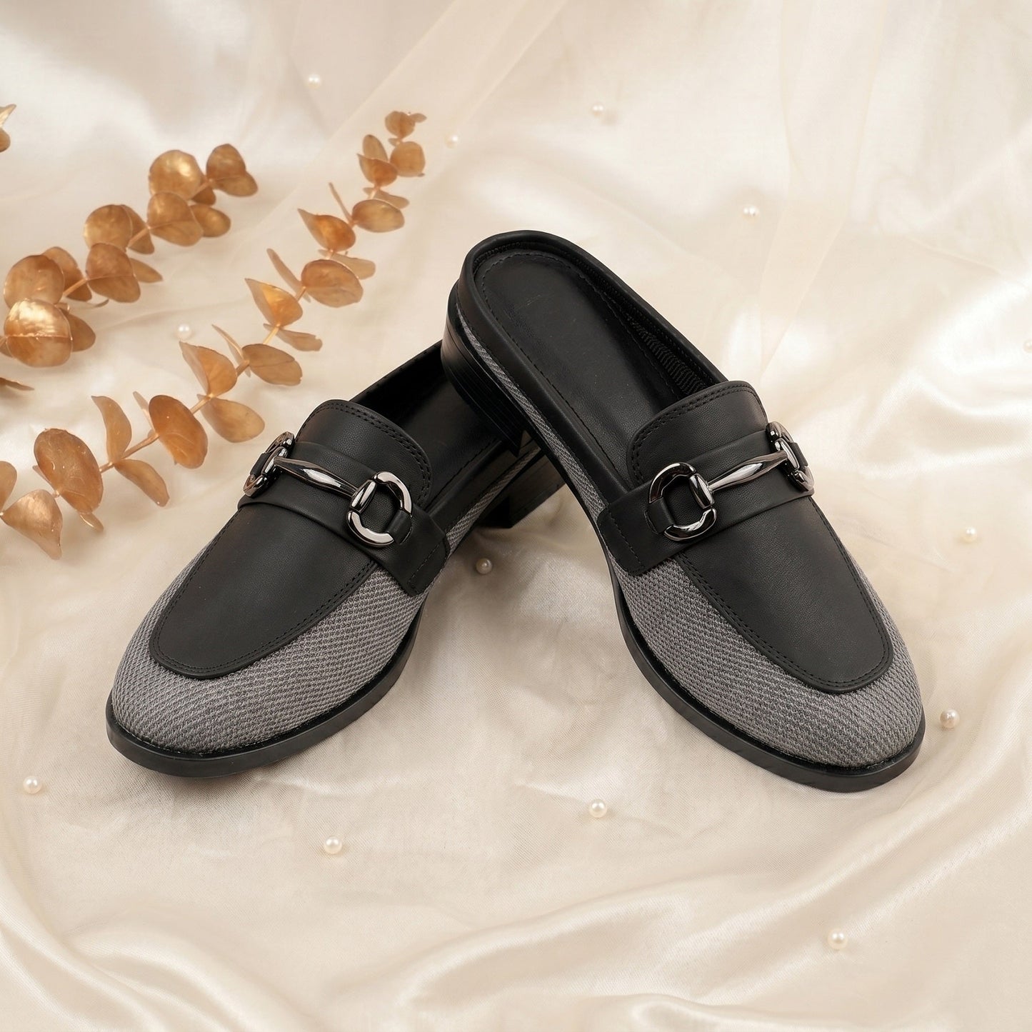 Black and gray loafers with a decorative buckle on a beige background