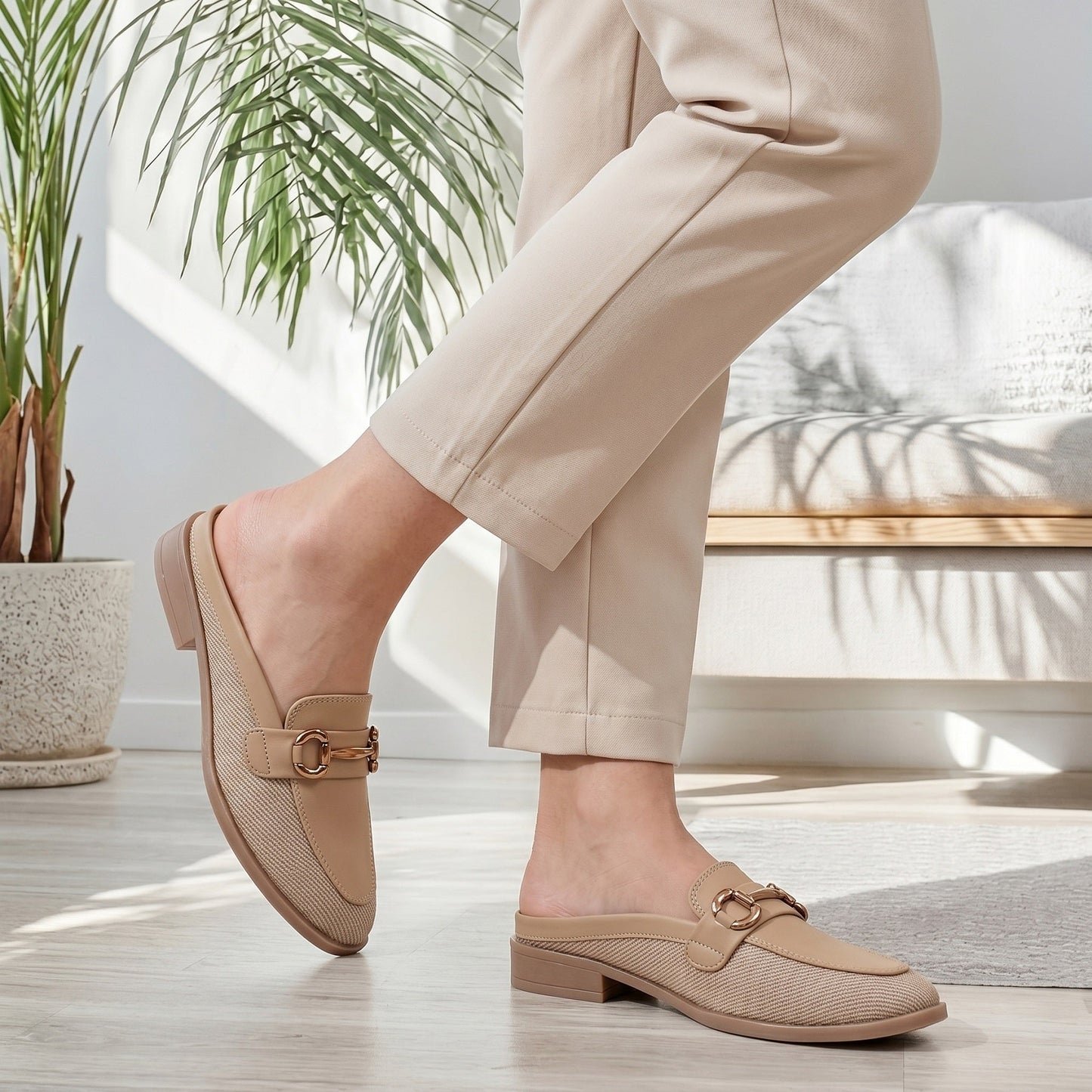 Person wearing beige loafers and pants in a bright room with plants.