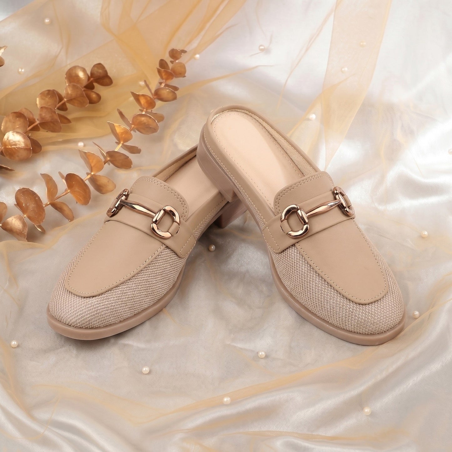 Beige loafers with gold buckles on a decorative fabric background