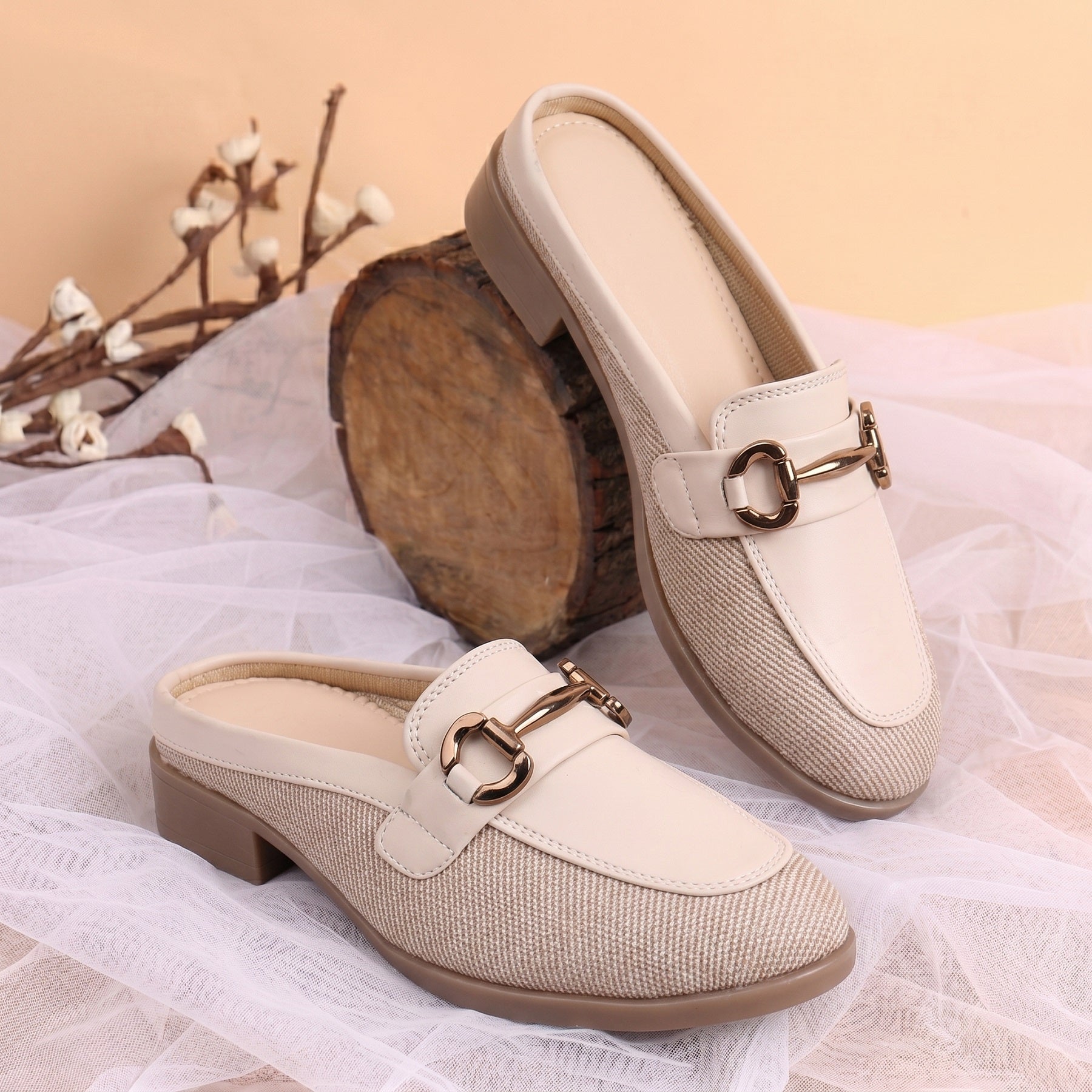 Pair of beige loafers with gold buckles on a soft fabric background