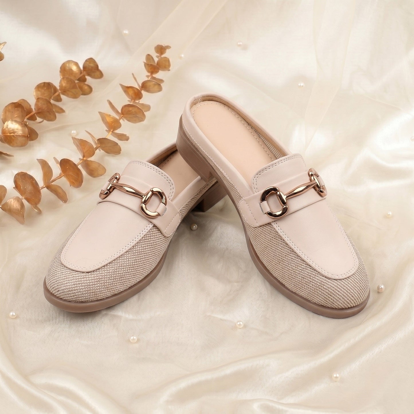 Pair of beige loafers with gold accents on a soft, light background