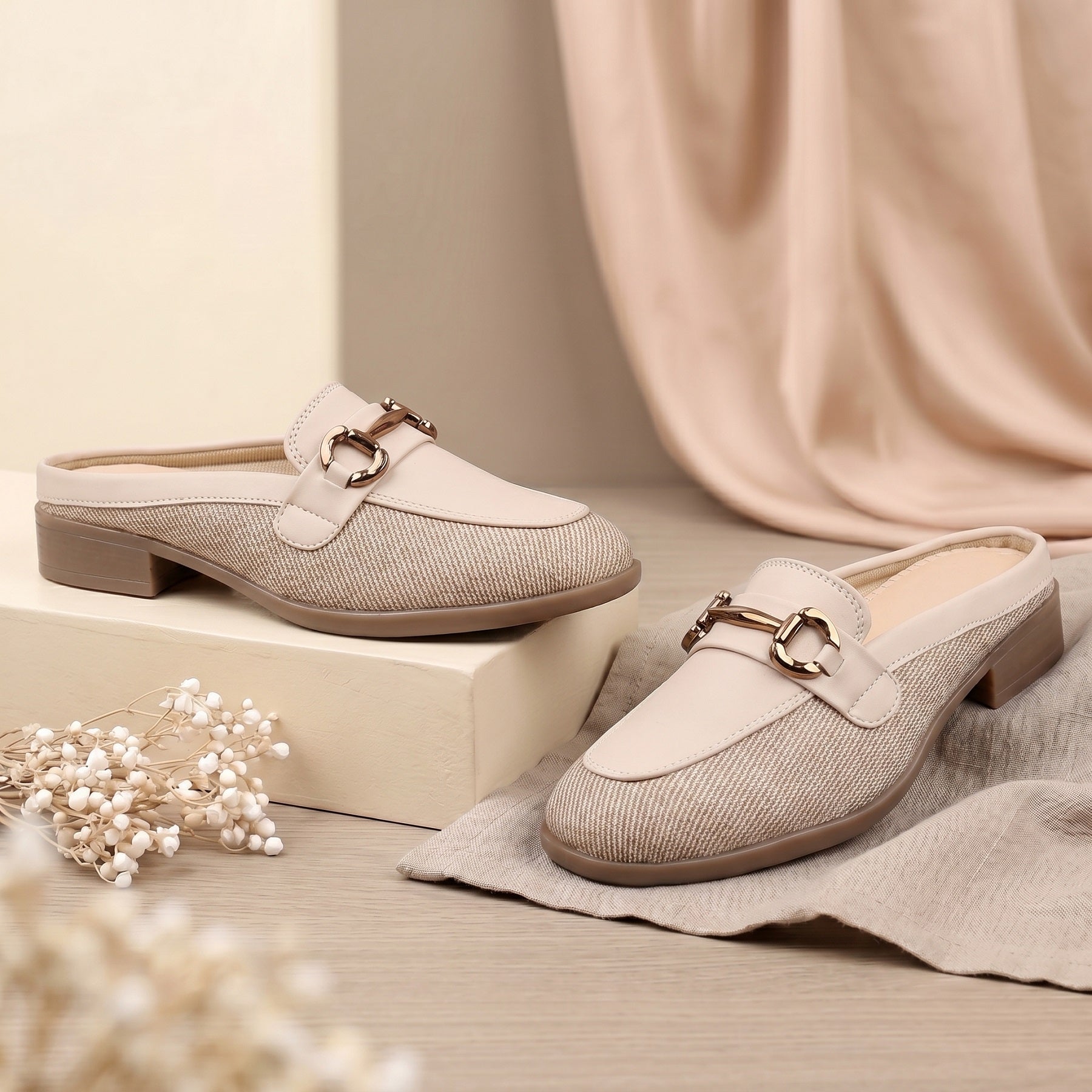 Pair of beige loafers with decorative buckles on a neutral background