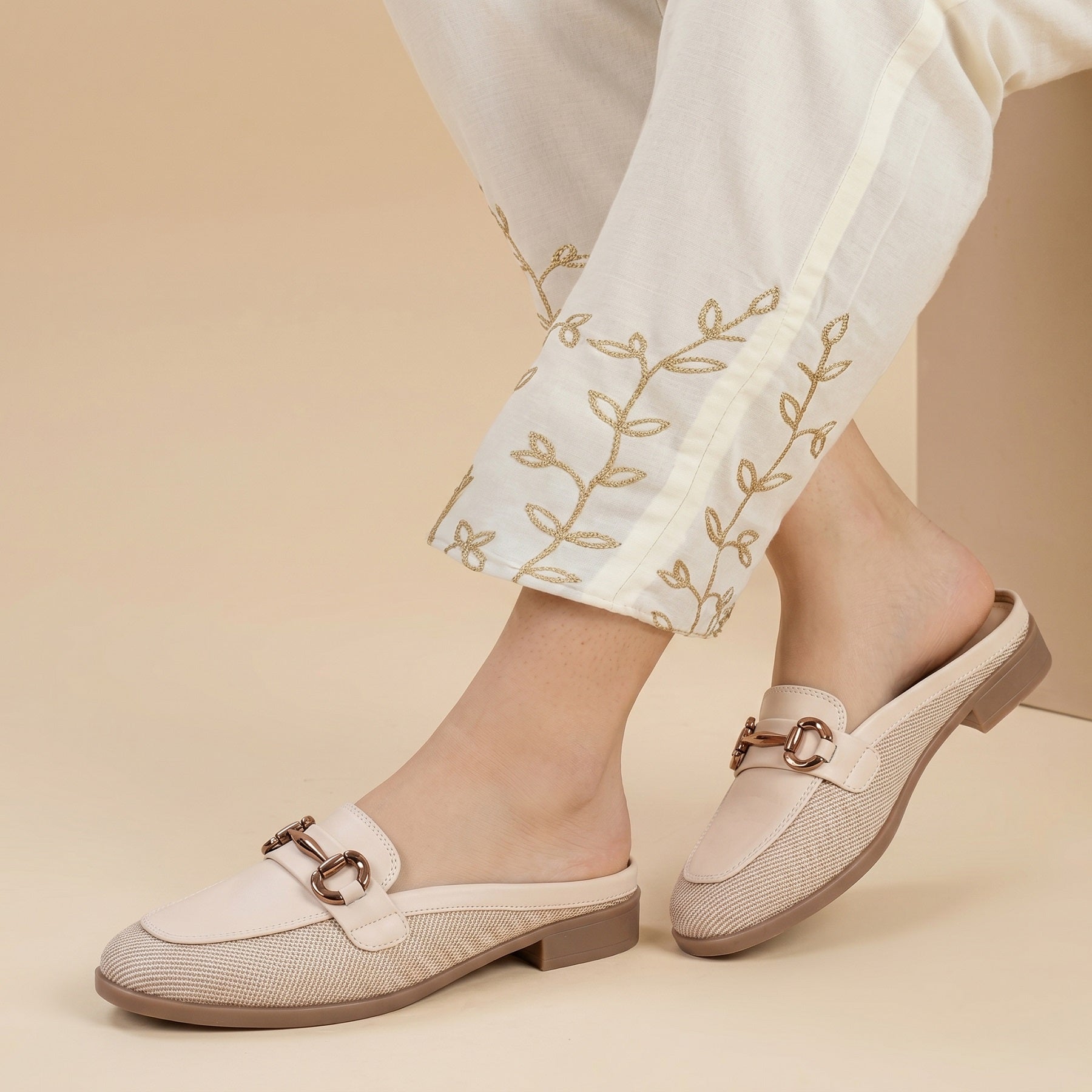White loafers with brown buckles worn with white pants on a beige background