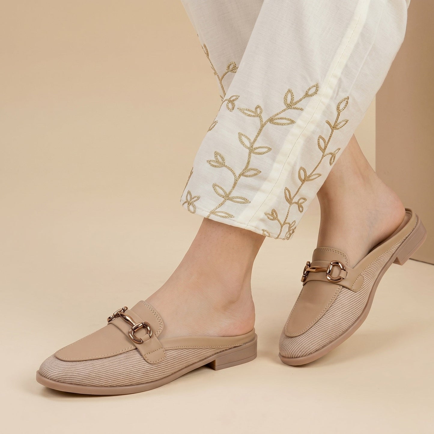 Beige loafers worn with white pants featuring embroidery on a beige background