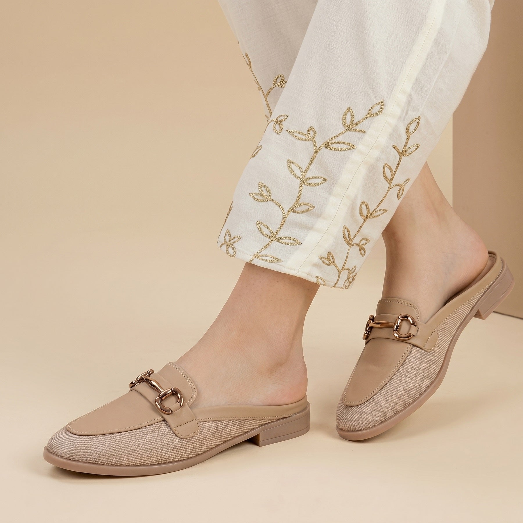 Beige loafers worn with white pants featuring embroidery on a beige background