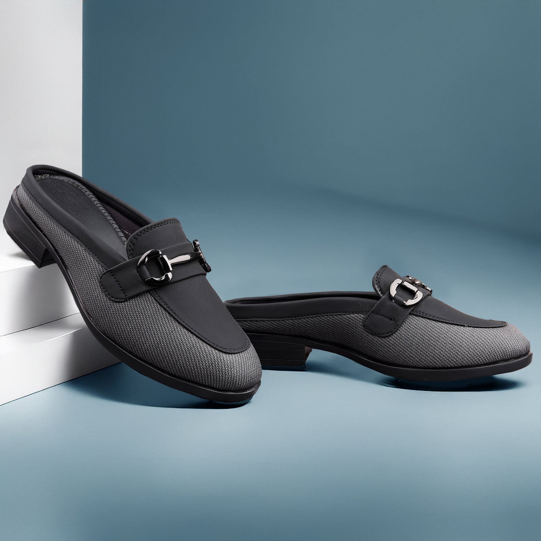 Pair of black loafers with a silver buckle on a blue background