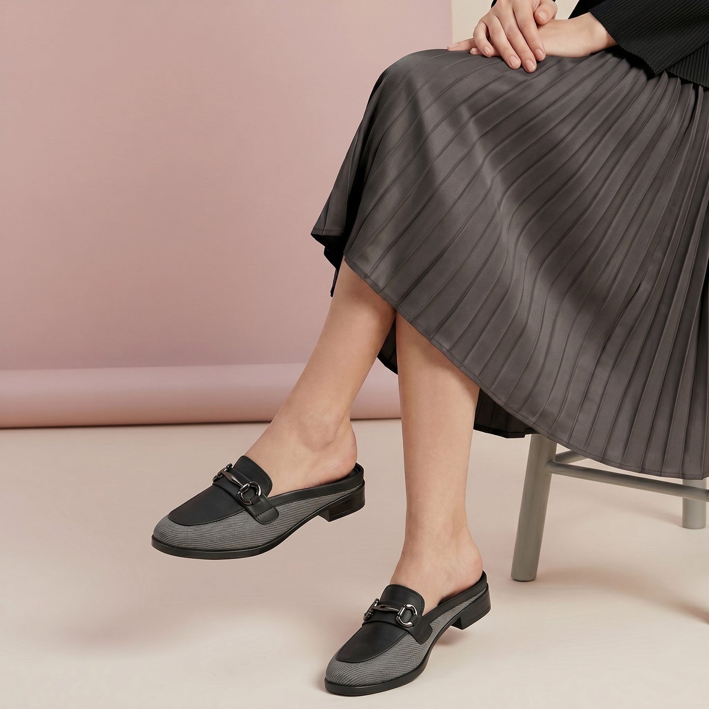 Person wearing gray loafers with black accents sitting on a chair against a pink wall.