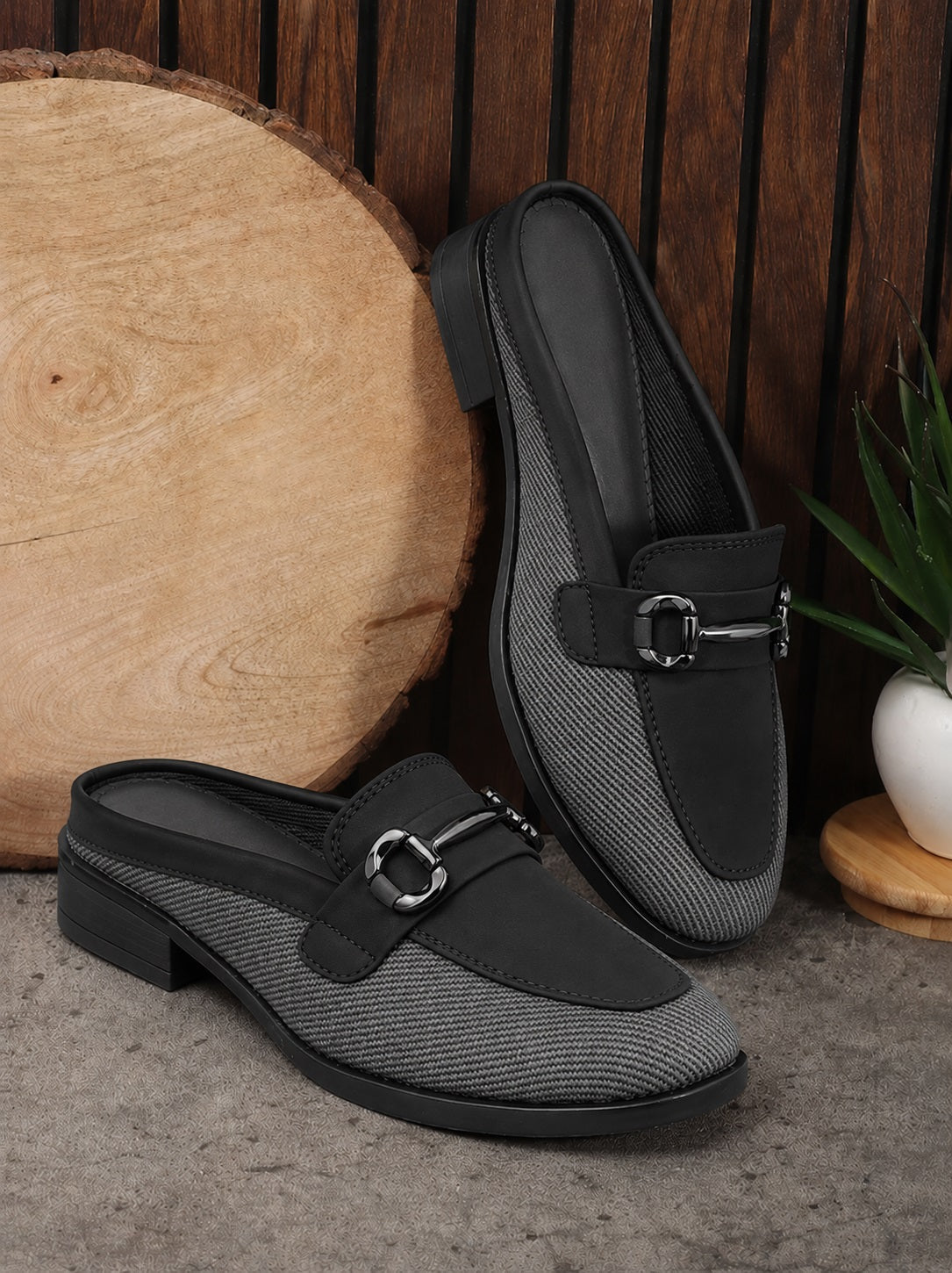 Black and gray loafers with a buckle on a wooden surface.
