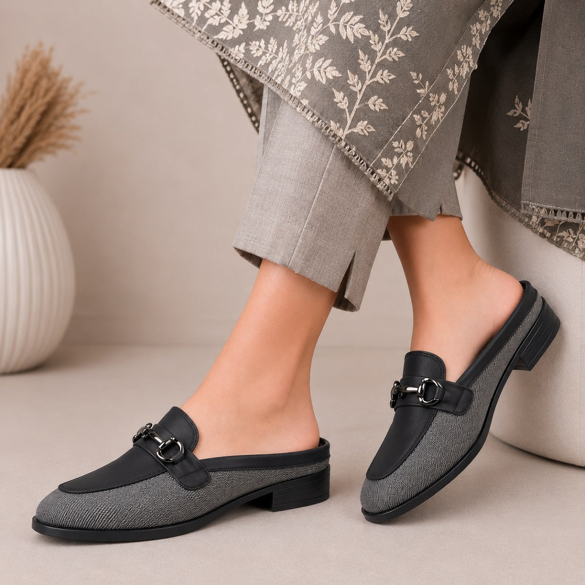 Gray loafers with black accents worn by a person sitting on a beige surface.