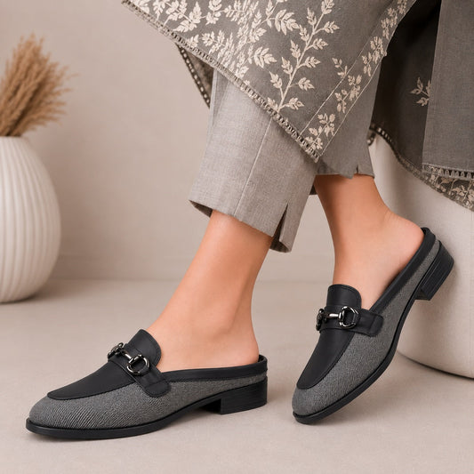 Gray loafers with black accents worn by a person sitting on a beige surface.
