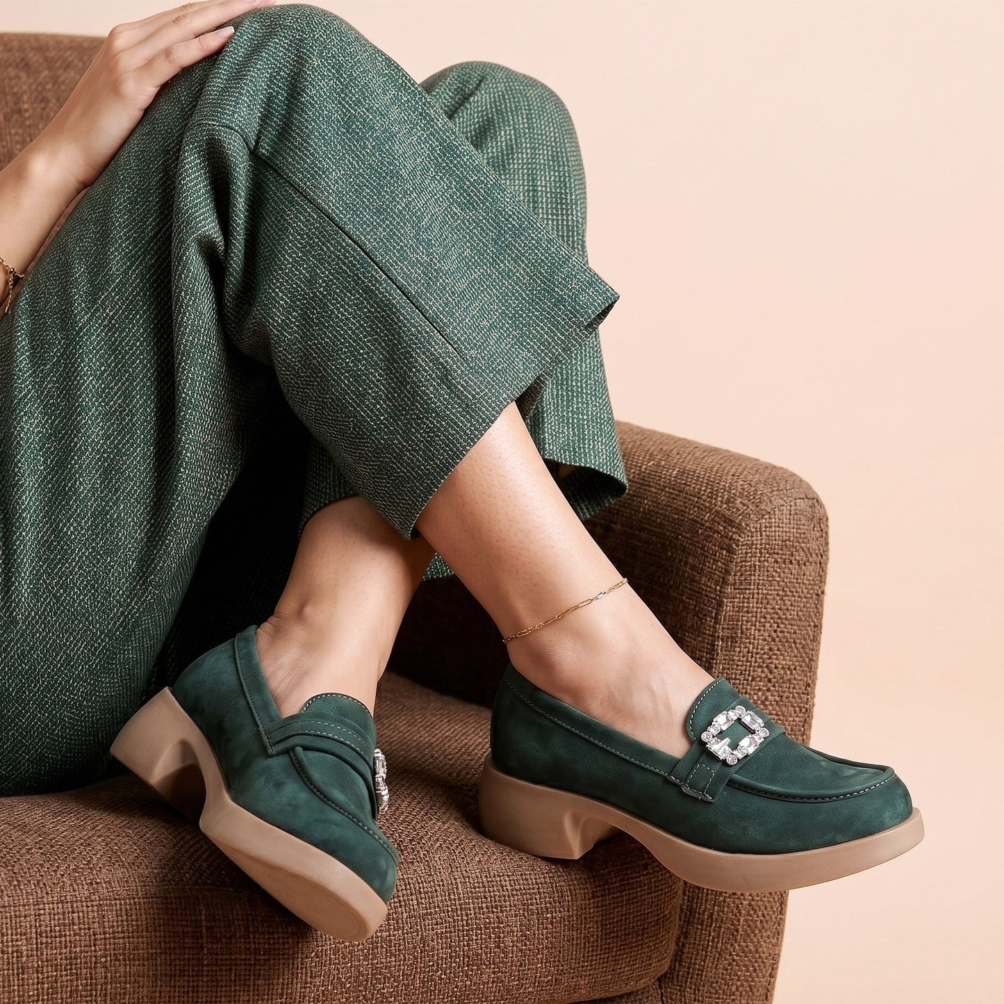Person wearing green loafers with a decorative buckle on a beige background
