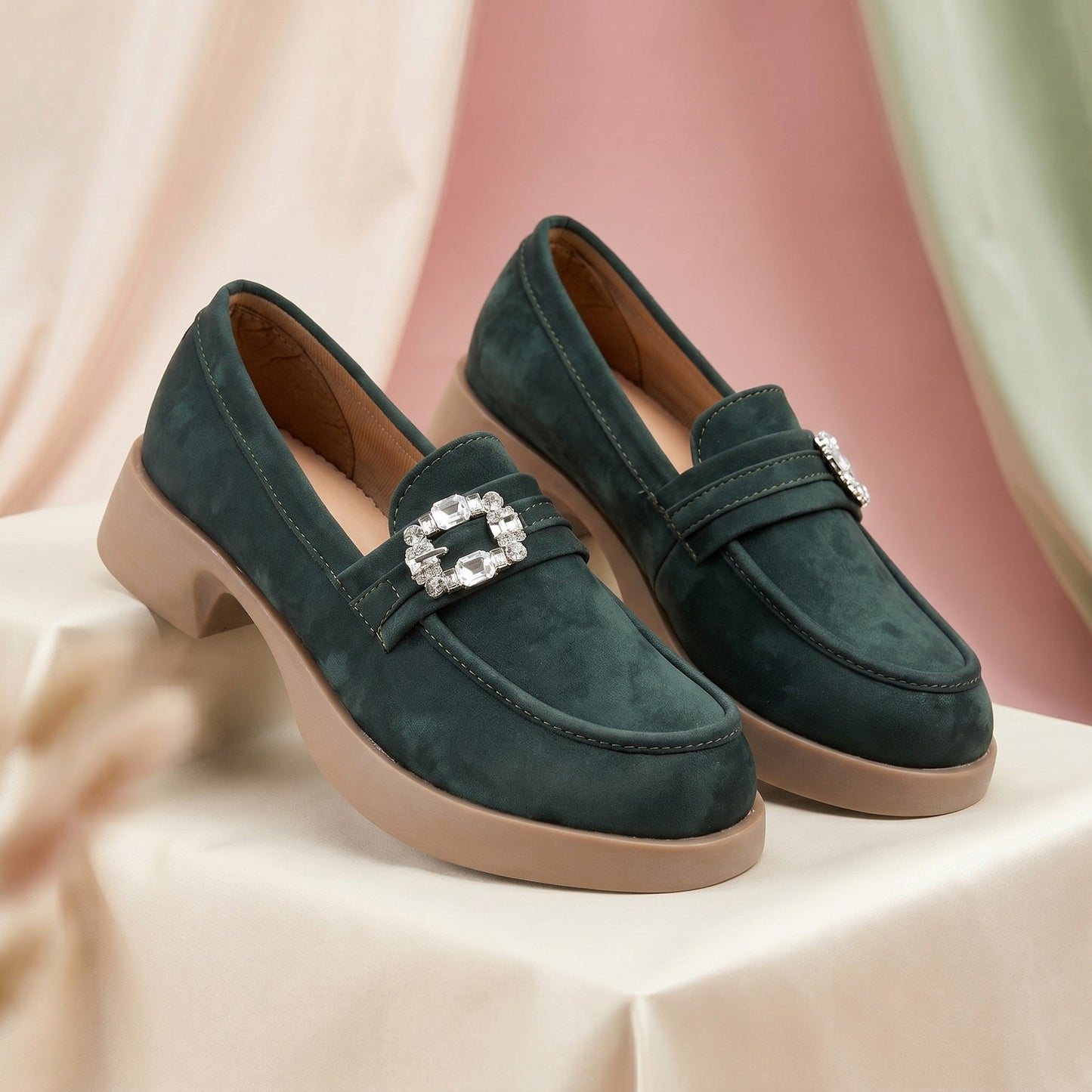Green loafers with a decorative buckle on a light pink background
