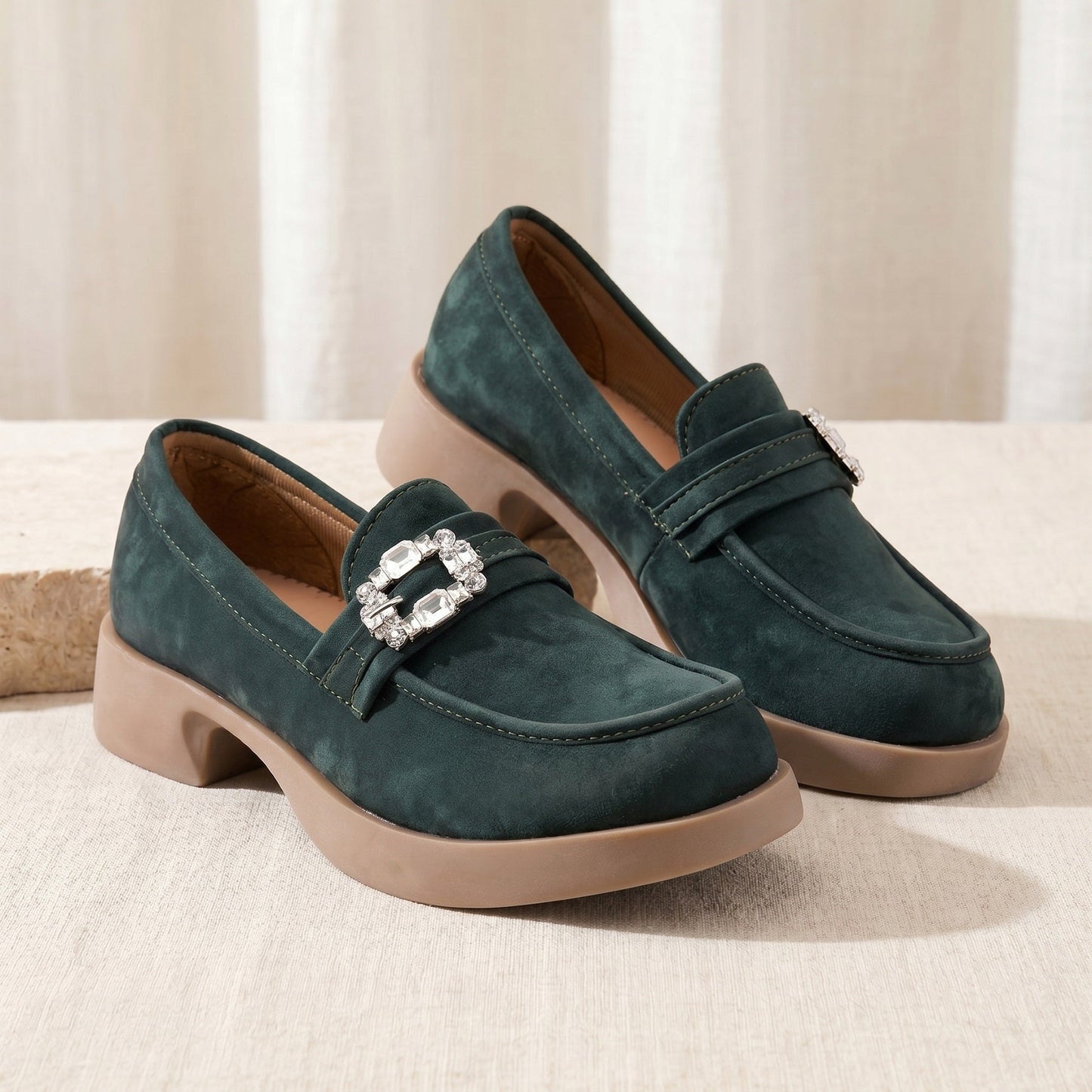 Pair of green loafers with a decorative buckle on a beige surface.