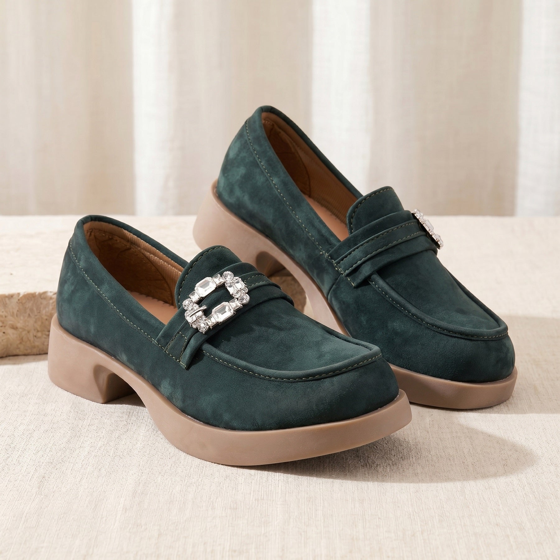Pair of green loafers with a decorative buckle on a beige surface.