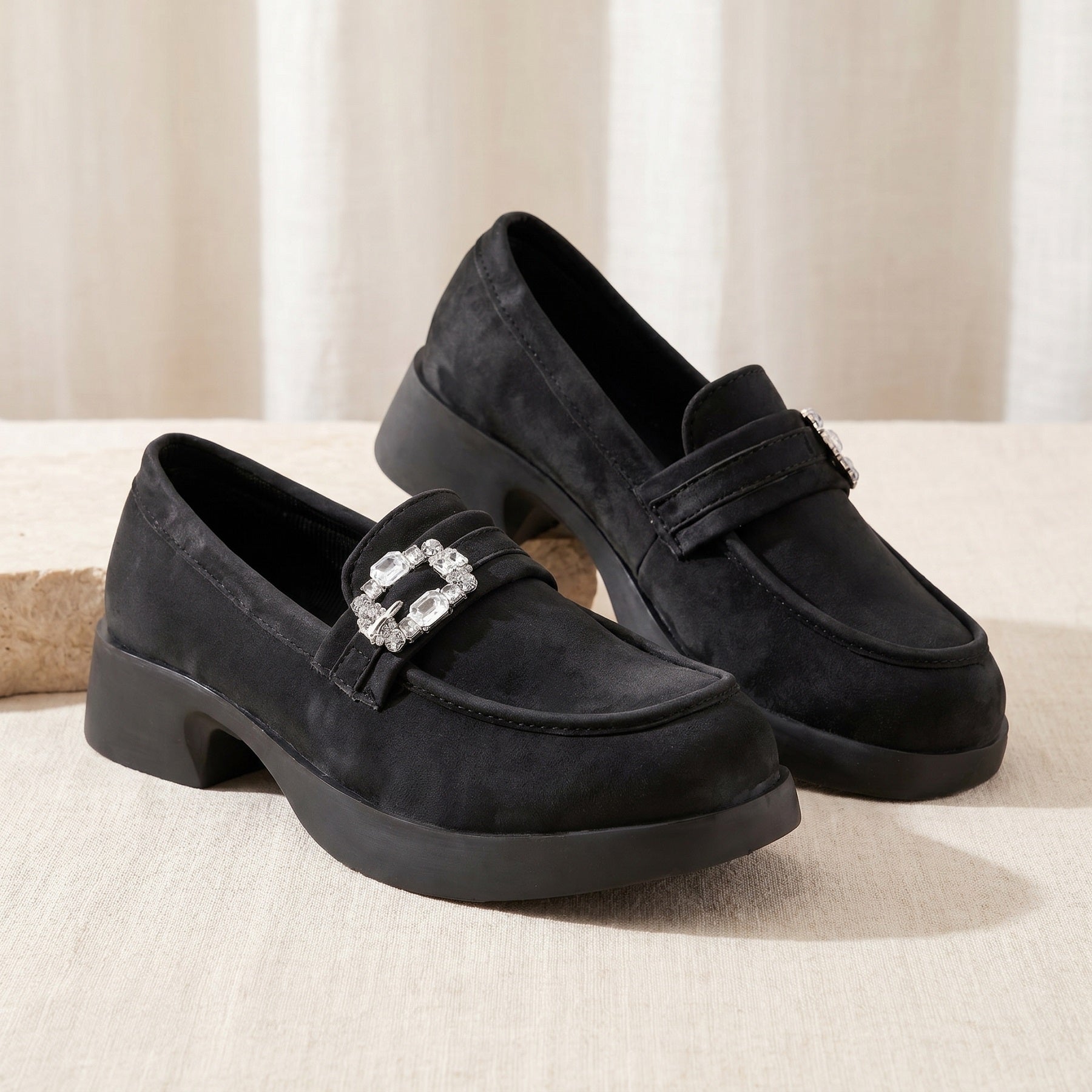 Pair of black loafers with a decorative buckle on a beige surface.