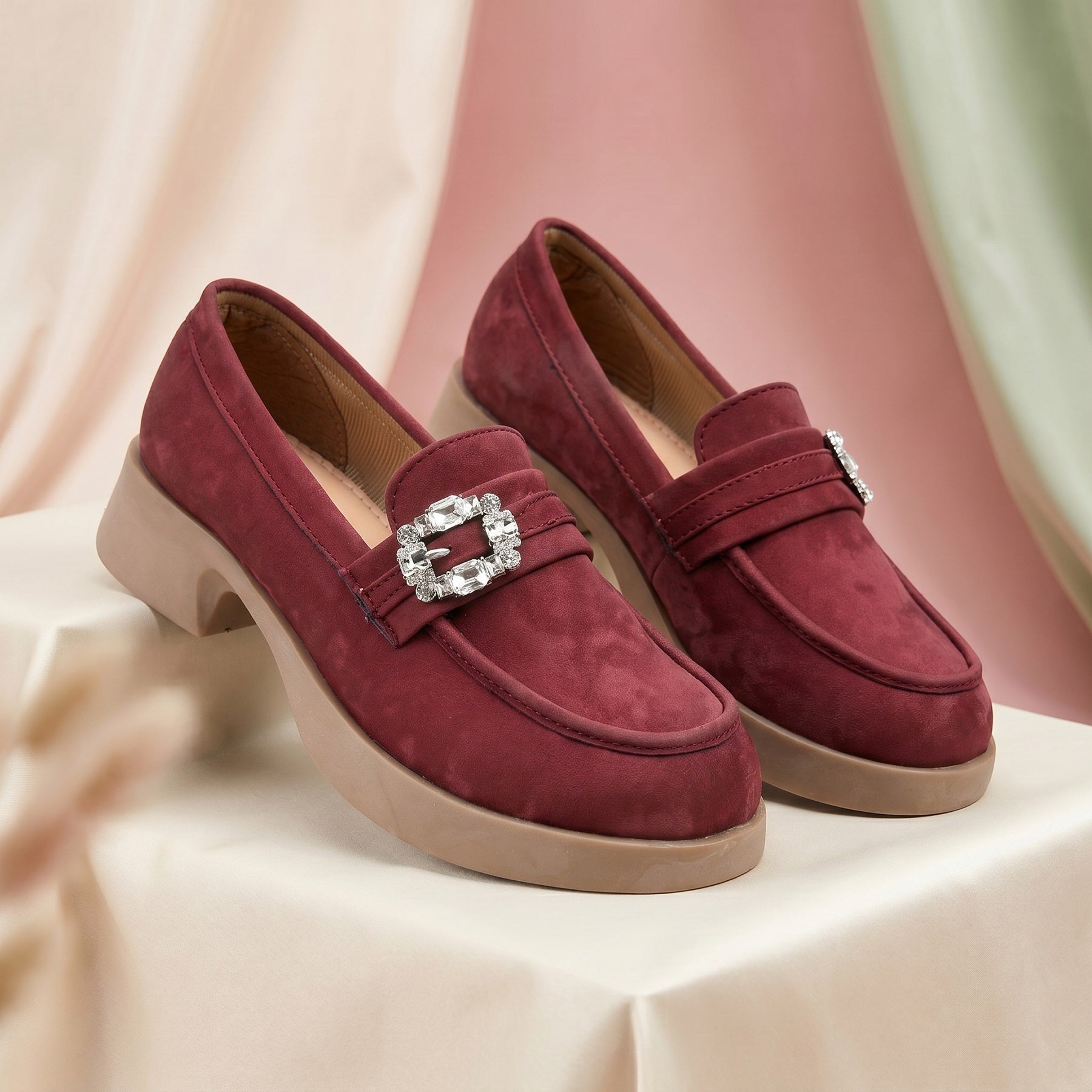 Pair of maroon loafers with a decorative buckle on a light background