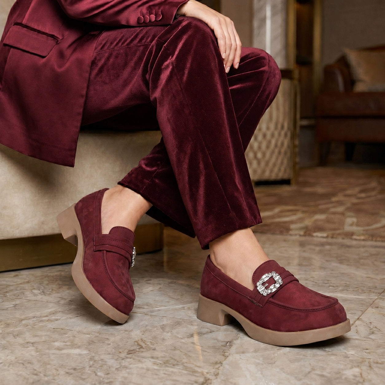 Person wearing burgundy loafers with a silver buckle on a marble floor.