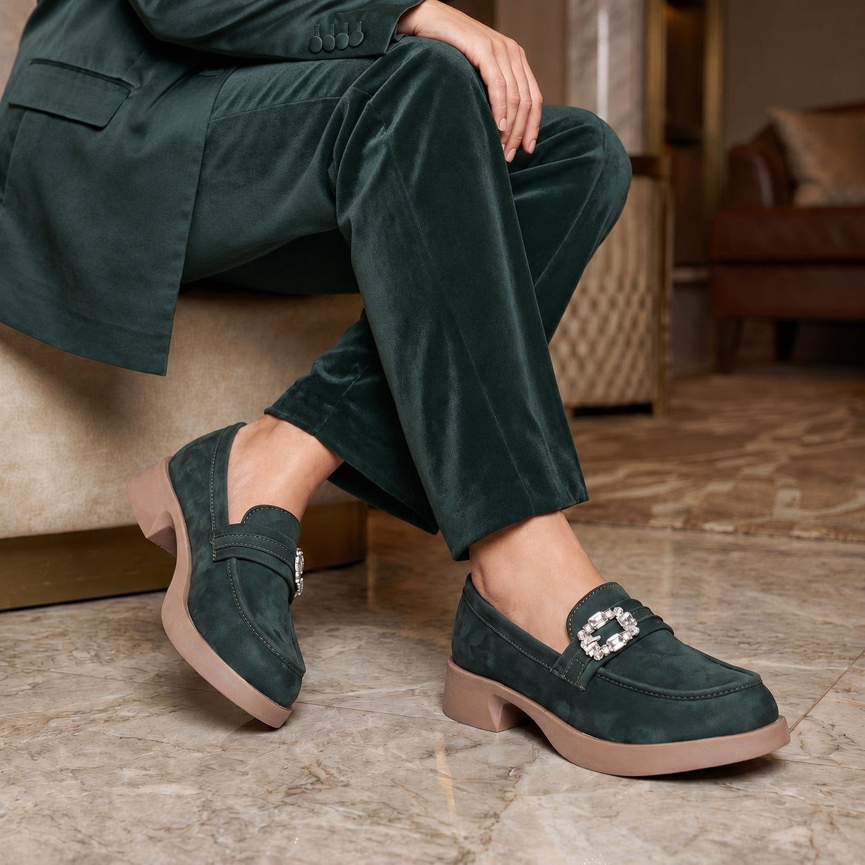 Person wearing dark green loafers with a decorative buckle in a living room setting.