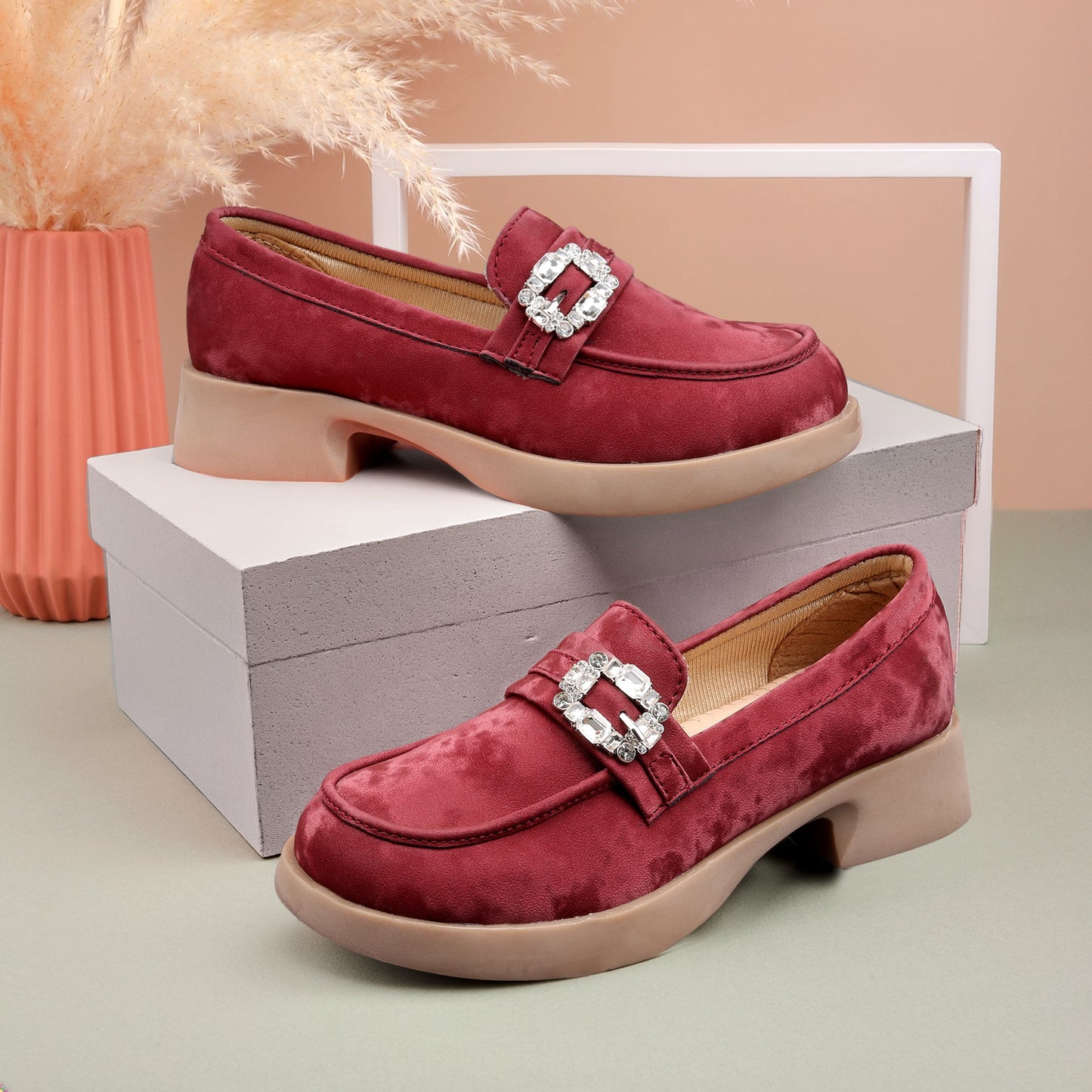 A pair of women's platform loafers in deep burgundy suede with a square crystal-embellished buckle, displayed on a white box and a light gray surface against a warm beige background.