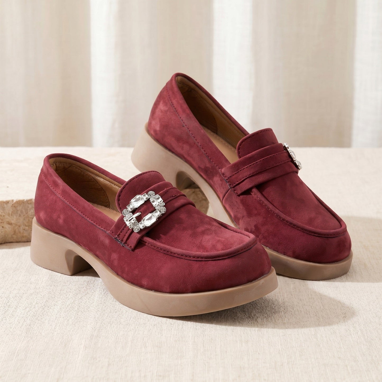 Pair of burgundy loafers with a decorative buckle on a light background