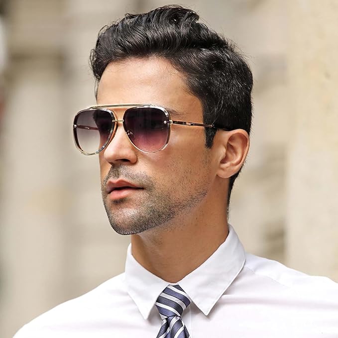 A man wearing aviator sunglasses with a gold-tone metal frame and gradient tinted lenses, dressed in a white collared shirt and a blue striped tie.